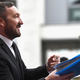 Ralph Ineson signing an autographs while wearing a black suit and smiling at the crowd.